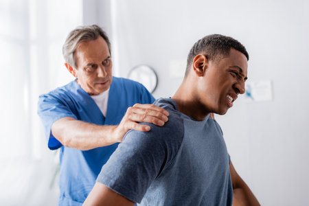 doctor working with injured african american man suffering from pain in clinic