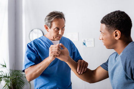 therapist working with injured arm of african american man in clinicの写真素材