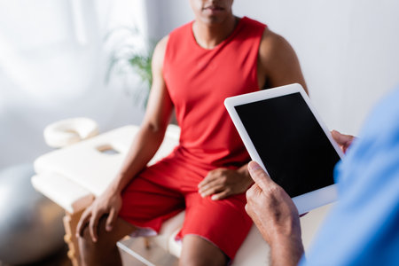 cropped view of doctor holding digital tablet with blank screen near african american patient in sportswear on blurred backgroundの写真素材