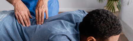 partial view of chiropractor working with young african american patient in clinic, bannerの写真素材