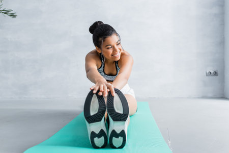 happy african american woman looking away while doing seated forward bend exercise on fitness matの写真素材