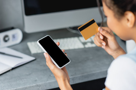 partial view of african american woman holding smartphone with blank screen and credit card, blurred foregroundの写真素材