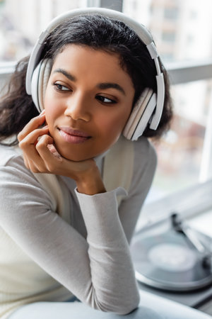 pensive african american woman listening music in wireless headphones at homeの写真素材
