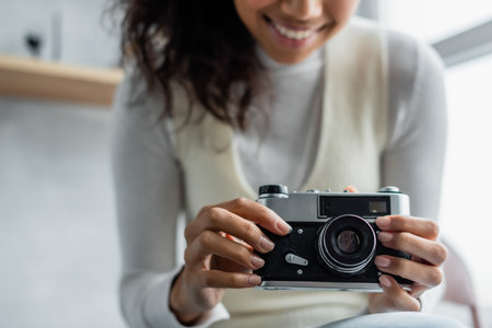 cropped view of smiling african american woman holding vintage photo camera, blurred backgroundの写真素材