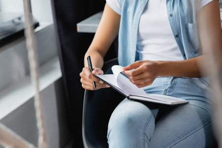 cropped view of african american woman holding notebook and pen while sitting at homeの写真素材