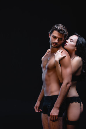 seductive woman embracing shoulders of sexy young man isolated on blackの写真素材