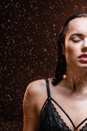 sensual woman in black lace bra with closed eyes under falling rain on dark backgroundの写真素材