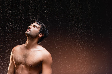 shirtless man with muscular torso standing on dark background under falling rainの写真素材