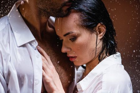 young woman leaning on chest of wet man under falling rain on dark backgroundの写真素材