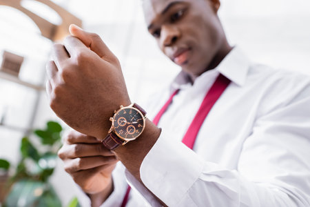 Wristwatch on hand of african american businessman on blurred background at homeの写真素材