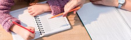Cropped view of mother pointing with pencil near daughter writing in notebook on desk, banner