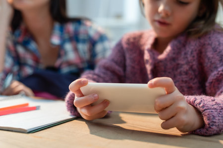 Cropped view of daughter using smartphone near mother at desk on blurred backgroundの写真素材