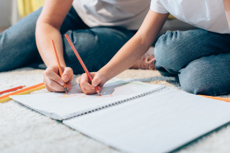 Cropped view of mother and daughter drawing with colored pencils in copy book on floor on blurred foregroundの写真素材