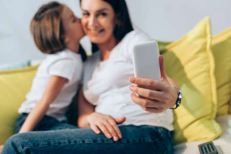 Daughter kissing smiling mother during selfie at home on blurred backgroundの写真素材