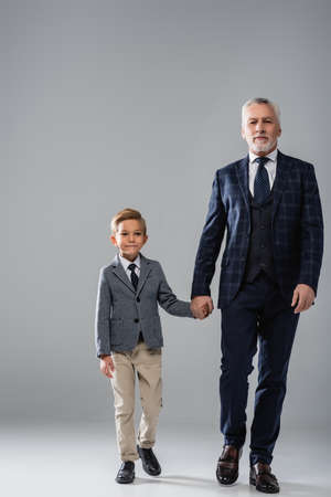 mature businessman holding hand of grandson while walking on grayの写真素材