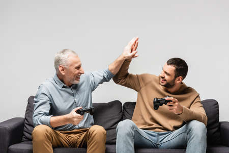 happy father and son giving high five while holding joysticks isolated on grayの写真素材