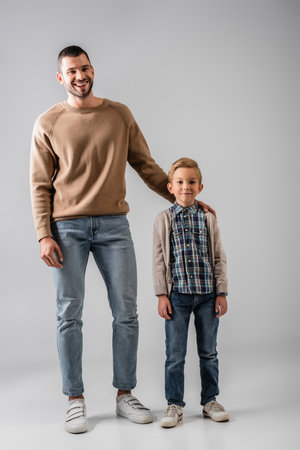 happy man hugging shoulder of son while standing together on grayの写真素材