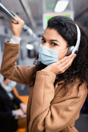 curly african american woman in medical mask listening music in subwayの写真素材