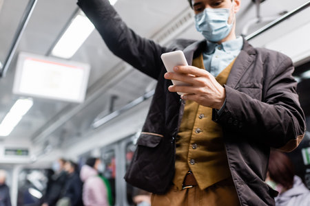 man in medical mask using smartphone while standing in wagon of metroの写真素材