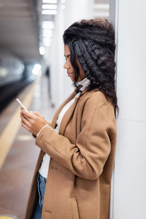 side view of curly african american woman using smartphone in subwayの写真素材