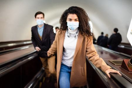 interracial man and woman in medical masks on escalator in subway