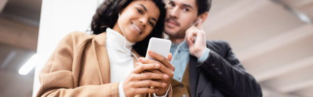 low angle view of multicultural couple with smartphone listening music in earphones in subway on...
