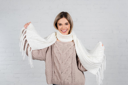 Smiling woman in knitted sweater holding scarf on white backgroundの写真素材