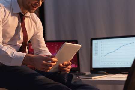 Cropped view of digital tablet in hands of businessman on blurred background in office in eveningの写真素材