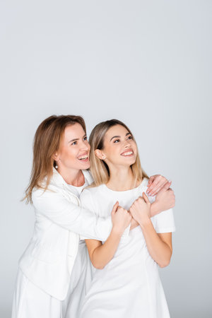 happy mother hugging young daughter isolated on gray, generation of womenの写真素材
