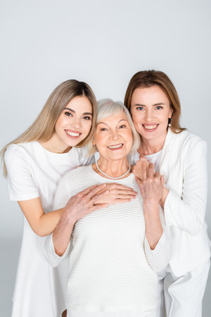 three generation of happy women smiling while looking at camera isolated on grayの写真素材