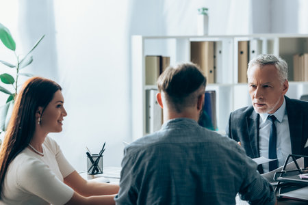 Investor talking with businessman near smiling businesswoman on blurred foreground