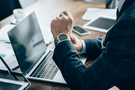 Cropped view of businessman sitting near devices with blank screen and papers in office