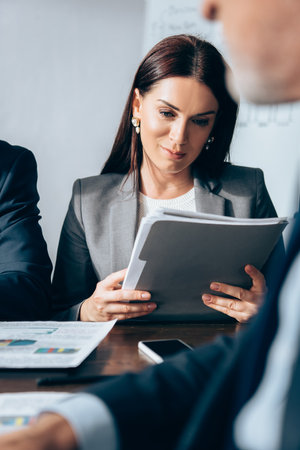 Businesswoman holding paper folder near investor on blurred foregroundの写真素材