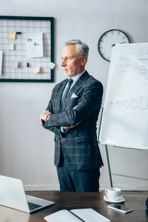Mature businessman standing near devices and cup in officeの写真素材