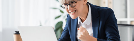 worried team leader in glasses cheering while looking at laptop, banner