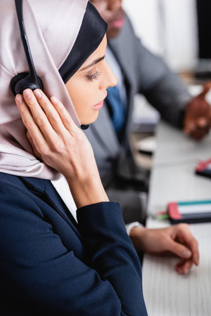arabian businesswoman touching headset near african american business partner of blurred backgroundの写真素材