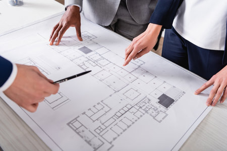 partial view of interracial business partners pointing at blueprint during meetingの写真素材