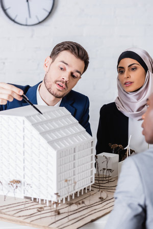 interpreter pointing with pen at model of building with solar batteries near arabian and african...