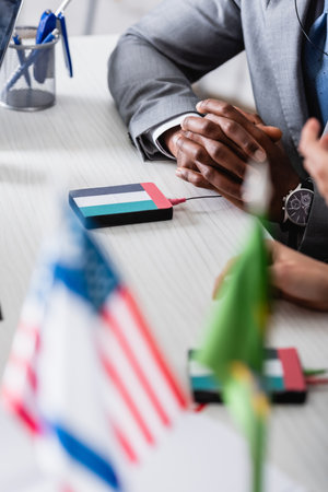 African american businessman cropped view of african american businessman sitting with clenched hands near digital translator with uae flag emblem, blurred foregroundの写真素材