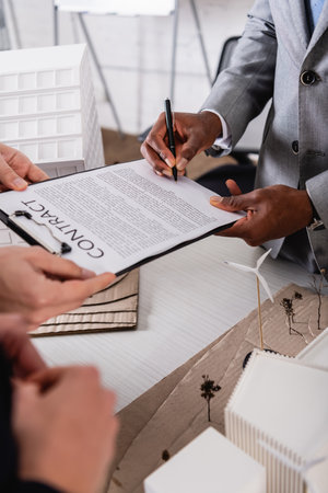 partial view of african american businessman signing contract near green power station model and...