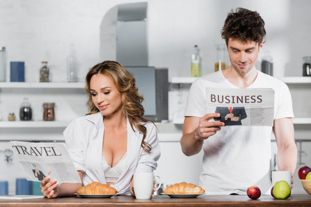 Sexy woman reading travel newspaper near boyfriend, coffee and breakfast in kitchenの写真素材