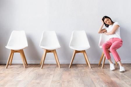 Tired asian woman waiting on chair in hallの写真素材