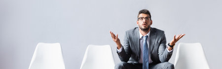 Businessman pointing with hands while waiting on chair in office, bannerの写真素材