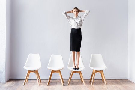 Businesswoman standing on chair and looking at camera in office hallの写真素材