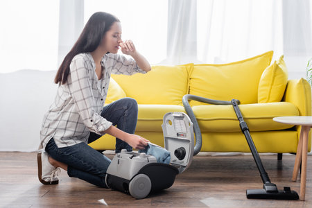 young woman suffering from allergy while holding dust bag near vacuum cleanerの写真素材