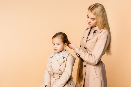 caring mother weaving braid on daughter isolated on beigeの写真素材