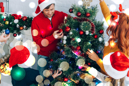 happy family in santa hats decorating christmas tree together at home, bokeh lights illustrationの写真素材