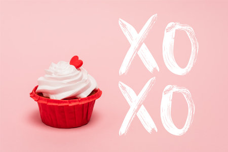 valentines cupcake with red heart near xoxo lettering on pink backgroundの写真素材