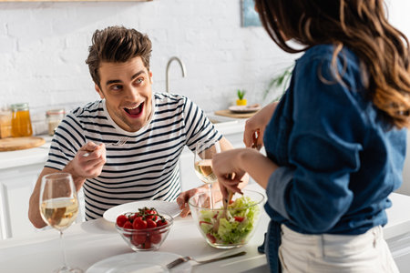 amazed man looking at woman serving salad in kitchen on blurred foregroundの写真素材