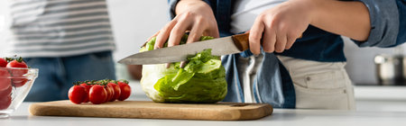 partial view of woman cutting lettuce near ingredients on kitchen table and boyfriend on blurred background, bannerの写真素材